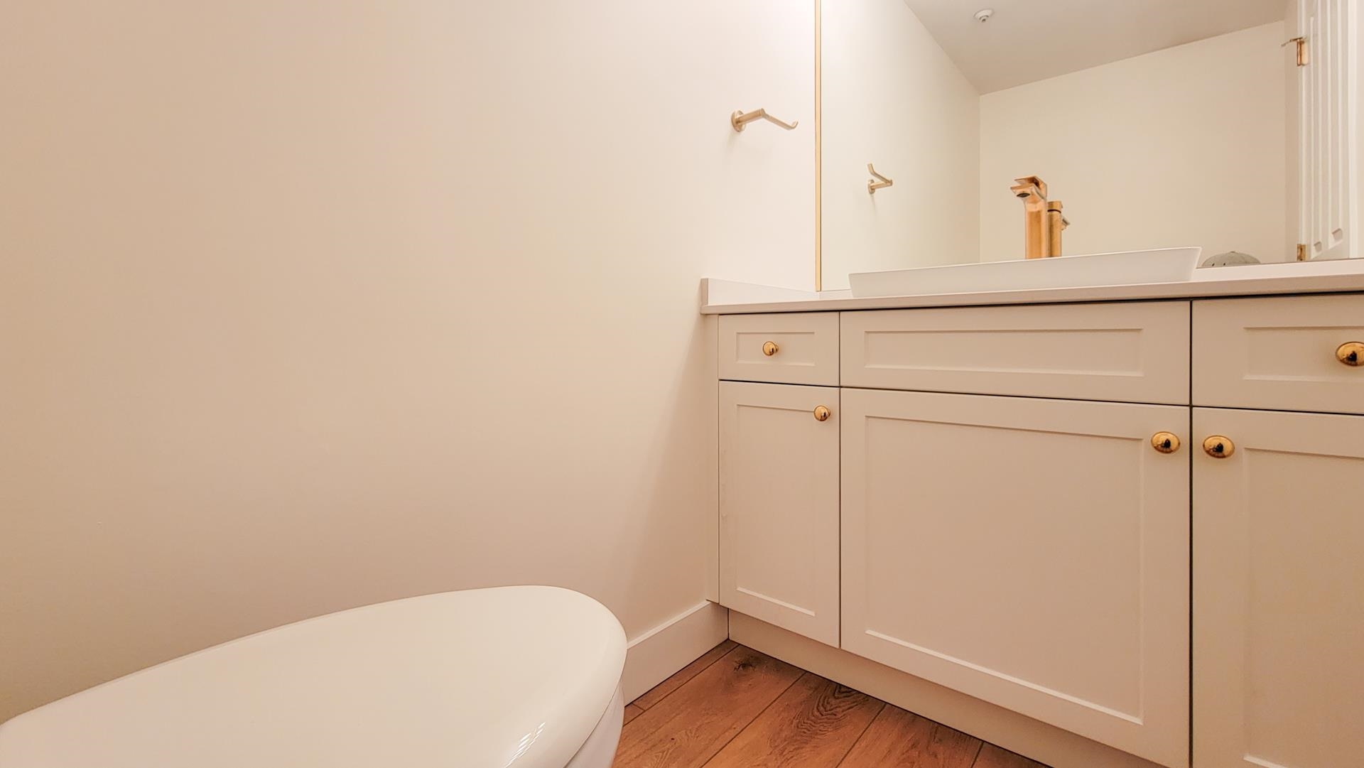 The powder room is located off of the foyer and is discretely tucked away.  The new cabinetry, sink toilet and gold fixtures are consistent with the primary bathroom